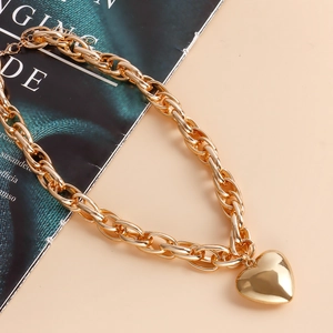 Macro shot of chunky gold O-chain necklace featuring a large 3D heart-shaped pendant