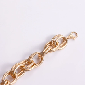 Macro shot of chunky gold chain bracelet with textured and polished links and lobster clasp