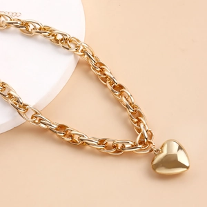 Close-up of golden O-chain necklace with a large heart pendant on a warm beige background
