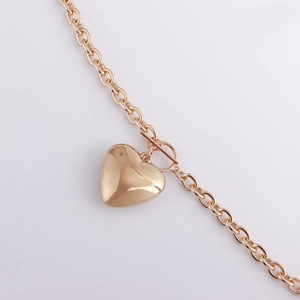 Close-up of a gold chunky chain with a polished heart pendant and decorative OT toggle clasp