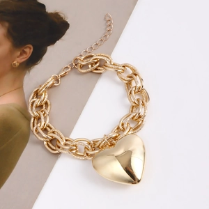 Macro detail of gold textured chunky chain and polished heart pendant on white background