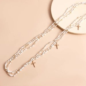 Detailed close-up of layered beaded waist chains with golden cross pendants on pink background