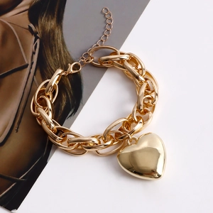 Detailed close-up of a chunky golden link bracelet featuring a polished heart charm