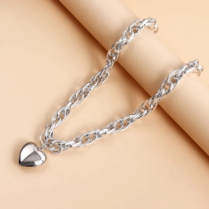 Close-up of a bold silver hollow link chain with a large polished heart pendant on a prop
