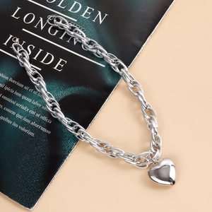 Detail of chunky silver O-chain necklace with a large polished heart pendant on a magazine