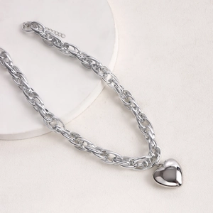 Detailed view of silver chunky O-chain necklace with polished heart pendant on white props