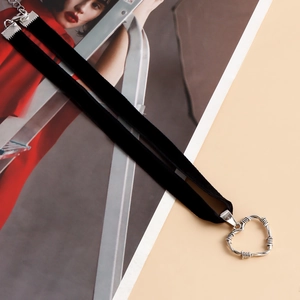 Dettaglio del choker in velluto nero con ciondolo a cuore strutturato su sfondo rosa chiaro