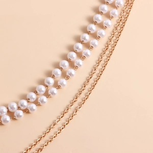 Detalle de cadena de pierna multicapa con perlas blancas y metal dorado para mujer