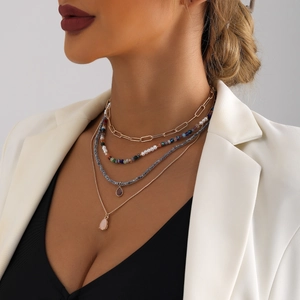 Dettaglio di una collana boho multistrato con perline colorate e ciondoli su abito bianco
