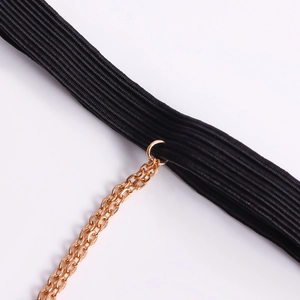 Dettaglio fascia elastica nera con anello dorato e catena sottile su gioielli da gamba