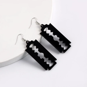 Macro shot of punk style black acrylic razor blade earrings on a textured display