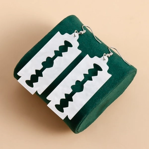 Macro shot of white resin razor blade earrings on a green velvet cylinder display stand