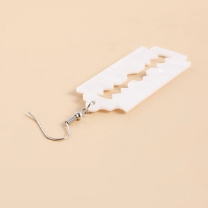 Detail of white acrylic razor blade earring with silver metal hook on beige background