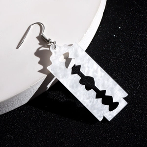 Detail of white marble acrylic razor blade pendant with silver ear hook on dark background