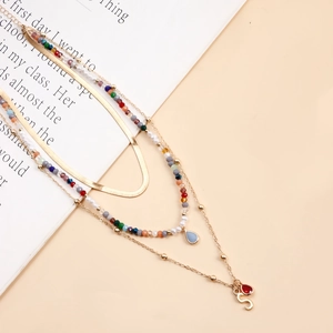 Dettaglio della collana dorata a strati con perline colorate, ciondolo lettera S e gemme