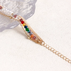Dettaglio del bracciale boho a strati con catena a serpente dorata, perle e perline