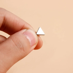 Close-up of a minimalist silver triangle pendant held between fingers to show small scale