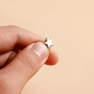 Macro shot of minimalist silver star stud earring held by hand on soft orange background