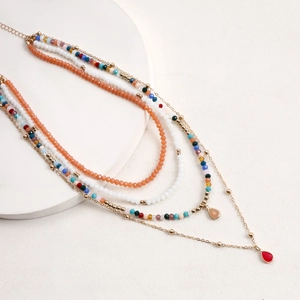 Dettaglio di una collana boho a strati con perline colorate e ciondoli a goccia arancioni