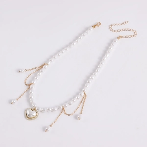 Detail van witte parels, gouden ketting en hartvormige hanger met strass en sluiting