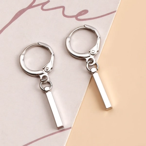 Détail de boucles d'oreilles créoles argentées avec un pendentif barre rectangulaire