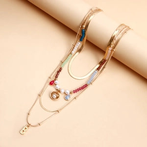Dettaglio collana a strati dorata con perline colorate, conchiglia e ciondolo lettera B