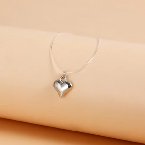 Macro view of polished silver heart pendant suspended on a transparent invisible chain