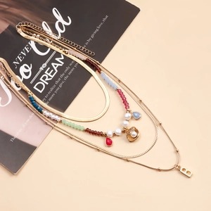 Dettaglio della collana a strati con perline, ciondolo a conchiglia dorato e lettera B
