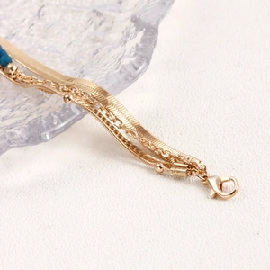 Dettaglio della collana multistrato dorata con catena a serpente e perla blu decorativa