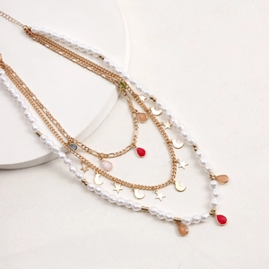 Dettaglio collana dorata multistrato con perle bianche, stelle e ciondoli a goccia colorati