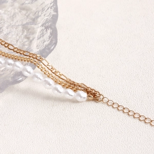 Dettaglio macro della collana multistrato dorata con perle bianche e chiusura regolabile