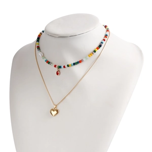 Dettaglio di una collana boho a strati con perline colorate e ciondolo a cuore dorato lucido