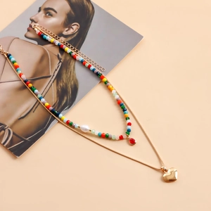 Dettaglio di una collana boho a strati con perline colorate e un ciondolo a cuore dorato