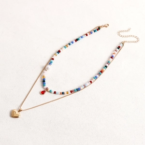 Dettaglio di collana a strati con perline colorate, cuore dorato e pendente a goccia rossa
