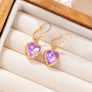 Macro view of gold heart earrings with purple crystal and delicate flower detail