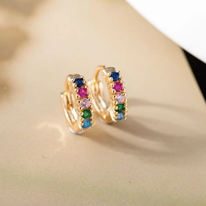 Macro shot of 18K gold huggie earrings with rainbow zircon stones on beige texture