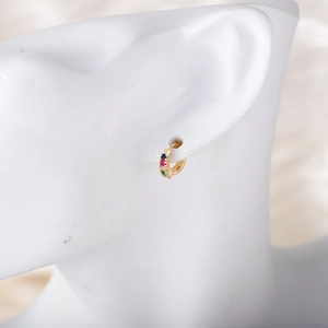 Detail shot of a small gold hoop earring with colorful rainbow zircons on a white model