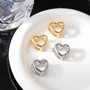 Dettaglio degli orecchini a cuore traforato in oro e argento su un vassoio di ceramica bianca