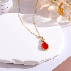 Macro view of gold plated teardrop necklace with red faux jade and sparkling diamonds