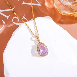Dettaglio del ciondolo a goccia con pietra rosa e collana in oro su pietra decorativa