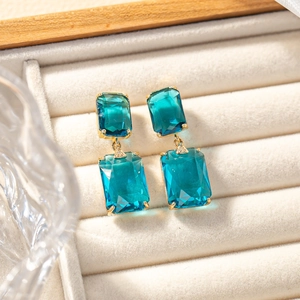 Macro detail of geometric gold earrings with aquamarine crystals and diamond accents