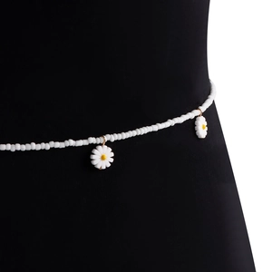 Détail de perles blanches et pendentifs marguerites jaunes sur une chaîne de taille