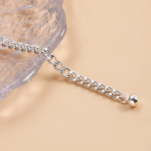 Détail d'une chaîne de corps argentée avec pendentif boule poli et mailles gourmettes