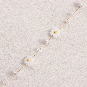 Nahaufnahme der Schleife-Halskette mit weißen Gänseblümchen, Perlen und Goldkette