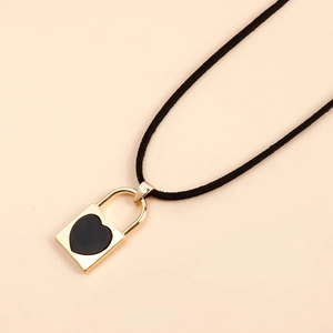 Detalle del colgante de candado de corazón dorado con incrustación negra en cordón de ante