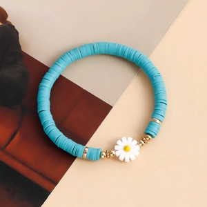 Macro detail of sky blue Heishi bead bracelet with golden accents and white daisy charm