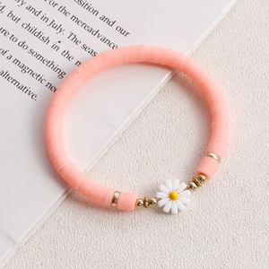 Detail of pink Heishi bead bracelet with a white daisy pendant on a white background