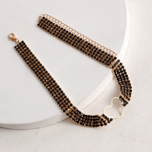 Close-up of black rhinestone choker with golden heart pendant on white stone base
