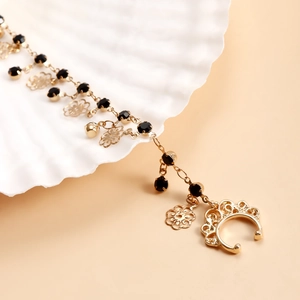 Detail of gold ethnic nose ring with black crystals, floral charms and a bell