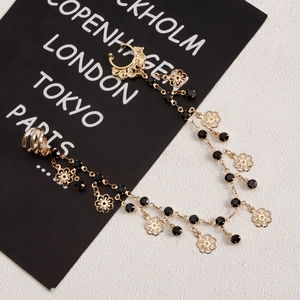 Close-up of gold chain earring with black beads, crescent moon clip, and flower pendant
